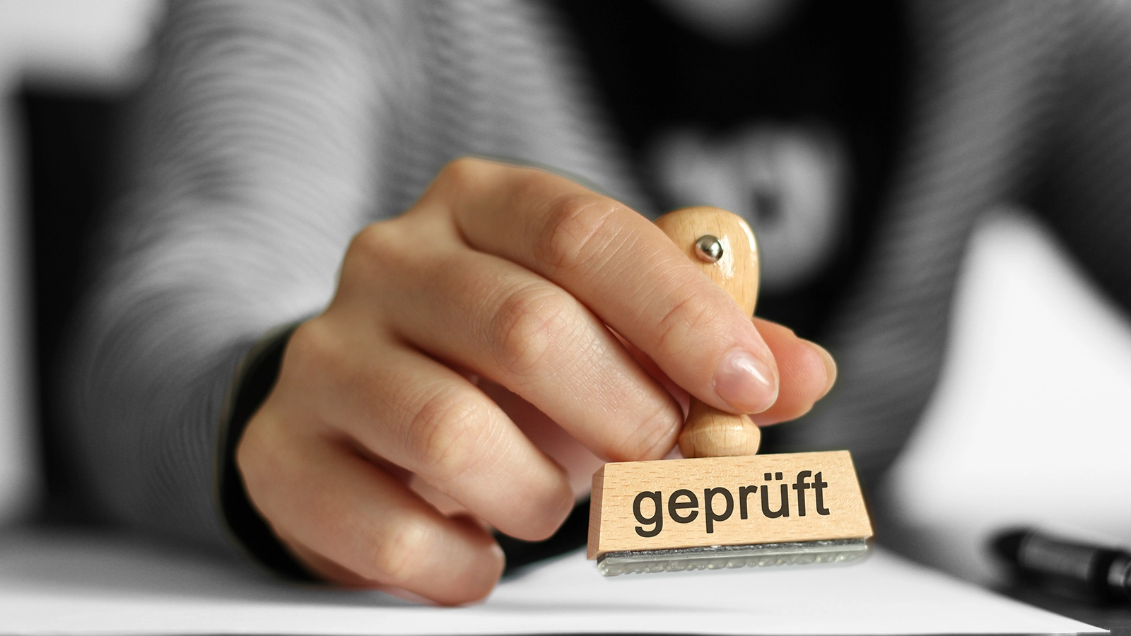 Eine Hand hält einen Stempel mit der Aufschrift geprüft.