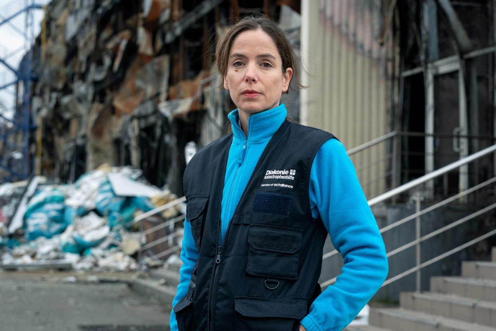 Portrait Anne Dreyer (Abteilungsleiterin Kommunikation und Fundraising, Diakonie Katastrophenhilfe). Im Hintergrund das von einem russischen Raketeneinschlag und Artilleriebeschuss am 25. Februar 2022 zerstörte Lebensmittelauslieferungslager.
