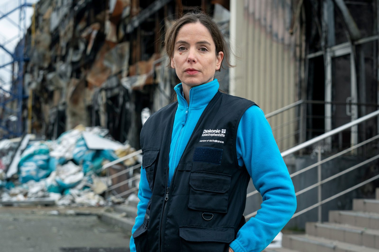 Portrait Anne Dreyer (Abteilungsleiterin Kommunikation und Fundraising, Diakonie Katastrophenhilfe). Im Hintergrund das von einem russischen Raketeneinschlag und Artilleriebeschuss am 25. Februar 2022 zerstörte Lebensmittelauslieferungslager.